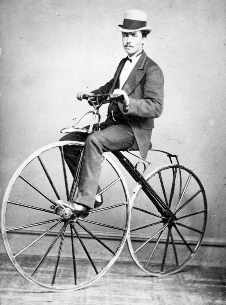 Man riding an early bicycle from the 19th century, showing the use of front-wheel pedals
